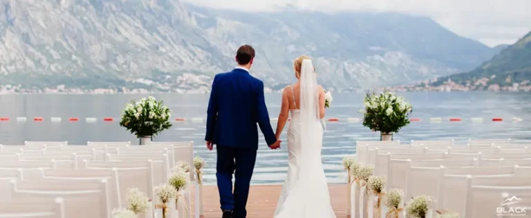 The groom and bride are walking down an aisle. A mountain and lake view in the background.